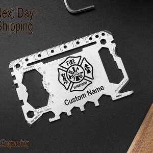 May include: A silver multi-tool credit card sized keychain with a fire department logo, a ruler, a bottle opener, and a box opener. The text "FIRE DEPARTMENT" and "Custom Name" are engraved on the tool.