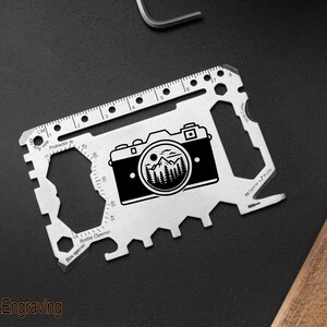 May include: A silver multi-tool card with a camera and mountain graphic. Features include a ruler, protractor, and bottle opener. The text "FranzEngraving" is at the bottom.