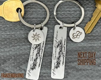 May include: Two silver keychains with engraved tags. One tag reads "Home Sweet Home Kristofer and Vihe" and has a floral design. The other tag reads "Home Sweet Home" and has a sun design. Both keychains have a small charm attached, one with a heart and the other with a sun.