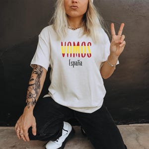 May include: A white t-shirt with a red and yellow graphic that says "Vamos Espa&ntilde;a".