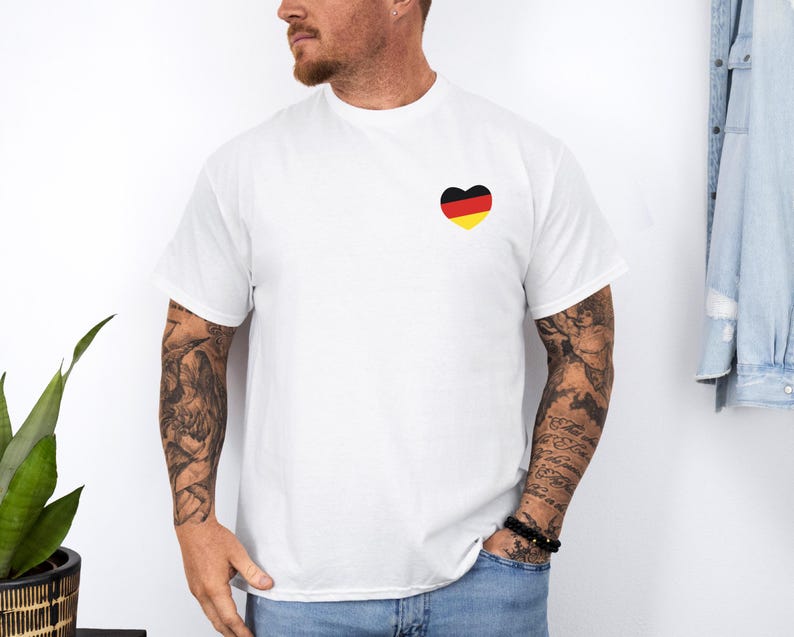 May include: White t-shirt with a black, yellow, and red heart-shaped design on the left chest. The heart design resembles the German flag.