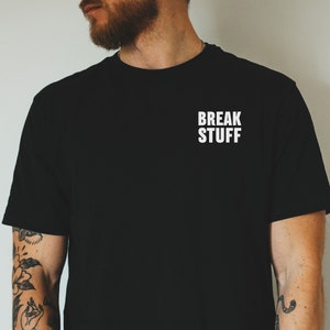 Pode incluir: T-shirt preto com o texto branco "BREAK STUFF" impresso na parte superior do peito. A camisa é de cor preta sólida e parece ser feita de um material macio. A t-shirt é um artigo de vestuário casual.