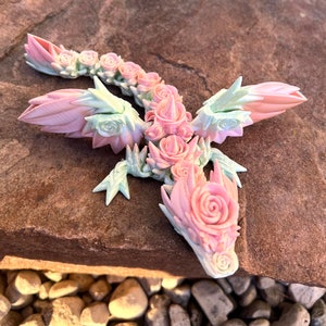 May include: A pink and green floral dragon sculpture with intricate details. The dragon is made of a smooth, glossy material and has a whimsical, fairy-tale aesthetic.