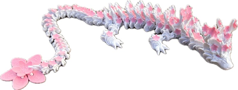 May include: A white and pink 3D printed dragon with a long tail and a flower at the end. The dragon is made up of many small, interlocking pieces.