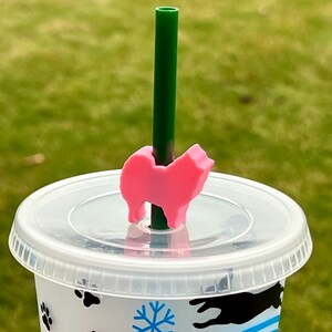 May include: A pink dog-shaped straw topper on a clear plastic cup with a green straw. The cup has a snowflake and paw print design.
