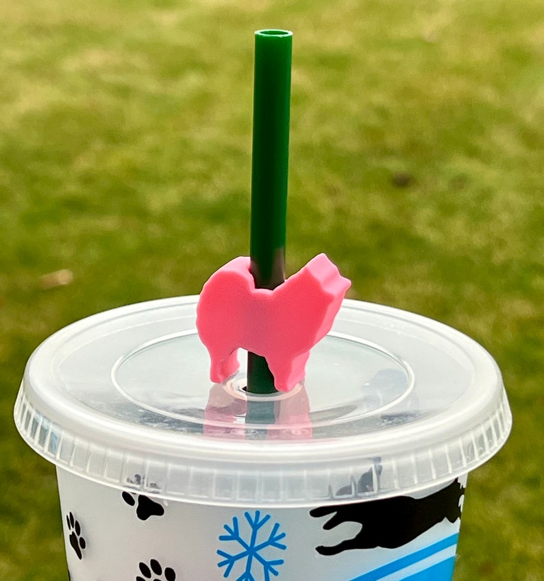 May include: A pink dog-shaped straw topper on a clear plastic cup with a green straw. The cup has a snowflake and paw print design.