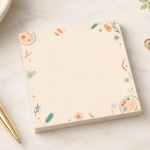 Può includere: Un blocco note quadrato con sfondo color crema caratterizzato da un bordo di piccole illustrazioni colorate di vari microrganismi, batteri e cellule in tonalità di blu, arancione e verde, disposte attorno allo spazio centrale vuoto.