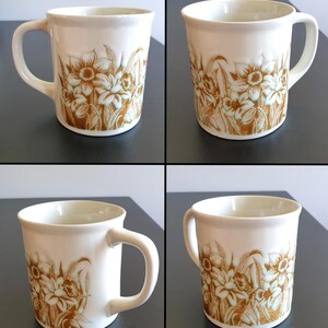 May include: Cream-colored ceramic mug with a brown floral design. The mug has a curved handle and a cylindrical shape. The floral pattern features stylized flowers and leaves. The mug is likely for beverages.