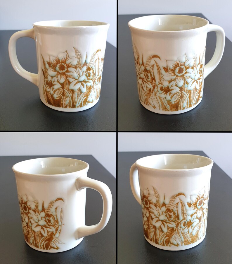 May include: Cream-colored ceramic mug with a brown floral design. The mug has a curved handle and a cylindrical shape. The floral pattern features stylized flowers and leaves. The mug is likely for beverages.