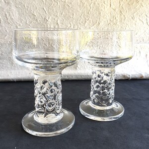 May include: Two clear glass goblets featuring smooth, wide bowls and thick, cylindrical stems with a distinct, raised, bubble-like textured pattern. Each goblet stands on a flat, circular base, showcasing a transparent design throughout.