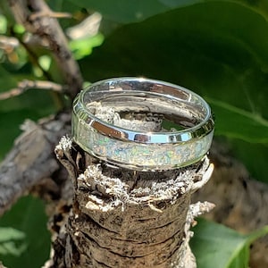 May include: A silver ring with a white opal inlay. The ring is sitting on a branch.