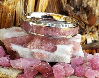 May include: A silver ring with a pink and white stone inlay. The ring is sitting on a piece of pink and white rock with smaller pink and white stones scattered around it.