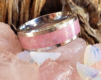 Puede incluir: Un anillo de plata con una incrustación de piedra rosa. El anillo está rodeado de piedras rosas y blancas.