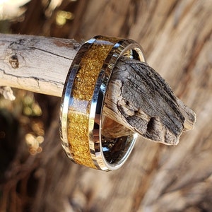 May include: A gold and silver ring with a textured gold band. The ring is on a piece of wood.