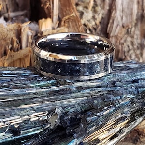 May include: A silver ring with a black inlay, set on a bed of blue-green crystals.