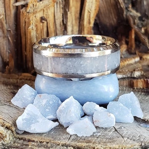 Może przedstawiać: Srebrny pierścionek z białym wkładką i niebieskim kamieniem. Pierścionek leży na kawałku drewna z rozrzuconymi wok&oacute;ł niebieskimi kamieniami.