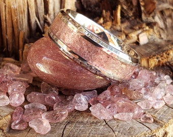 May include: A silver ring with a pink and white inlay, set on a bed of pink quartz stones.