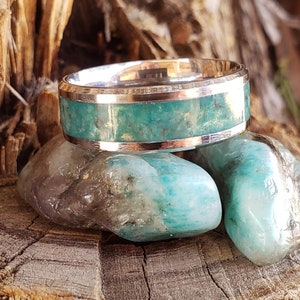 May include: A silver ring with a green stone inlay. The ring is sitting on two green stones.