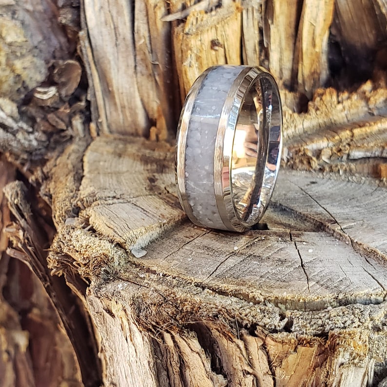 Może przedstawiać: Srebrny pierścionek z białym wkładką. Pierścionek leży na kawałku drewna.