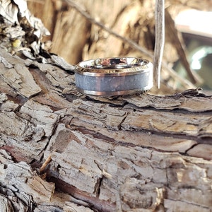 Może przedstawiać: Srebrny pierścionek z białym wkładką, na tle rustykalnego drewnianego tła.