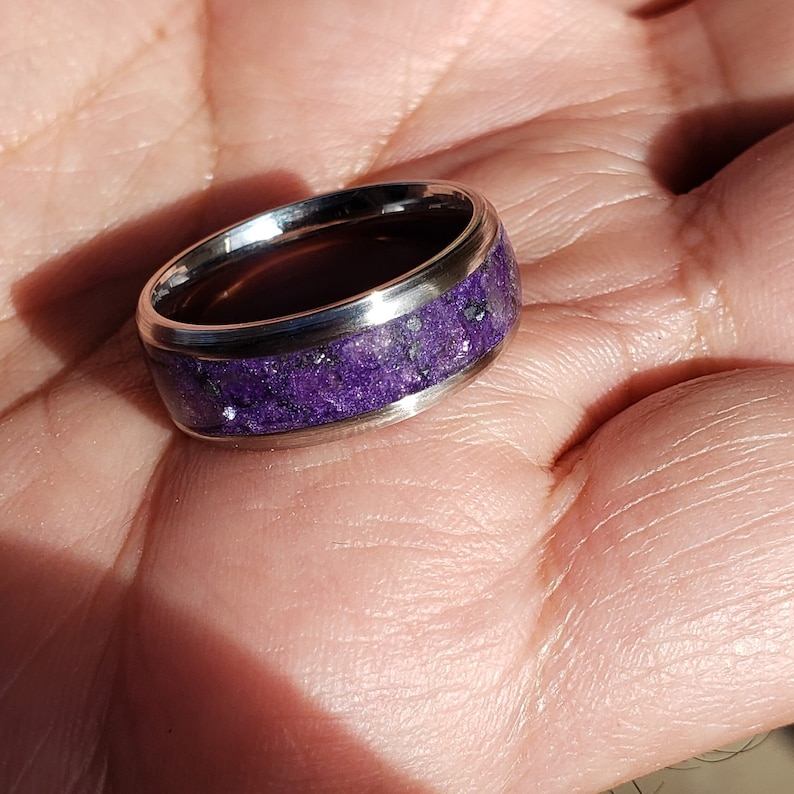 May include: A silver ring with a purple inlay. The inlay is made of small, crushed pieces of purple stone.