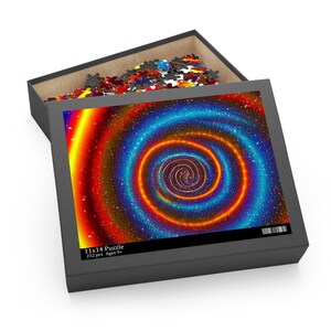 Peut inclure: Un puzzle de 252 pièces avec un motif de galaxie en spirale coloré. La boîte du puzzle est ouverte et montre les pièces à l'intérieur. La boîte porte l'inscription "11x14 Puzzle 252 pcs Ages 9+"