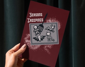 Può includere: Un biglietto di auguri bordeaux con la scritta "Seasons Creepings" e un tema di pasticceria spettrale. Il biglietto presenta una spatola e una teglia con disegni di scheletri, pipistrelli e gatti.