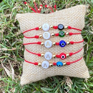 Puede incluir: Cinco pulseras de hilo rojo con cuentas doradas y cuentas de letras blancas que deletrean "AAAA" y "B". Cada pulsera tiene un amuleto de ojo turco azul, verde o negro.