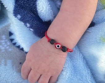 Puede incluir: Un brazalete de cuerda roja con una cuenta negra y un amuleto azul de ojo turco.