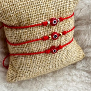 May include: Three red string bracelets with evil eye charms. Each bracelet has a gold bead and a silver bead.