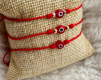 May include: Three red string bracelets with evil eye charms. Each bracelet has a gold bead and a silver bead.