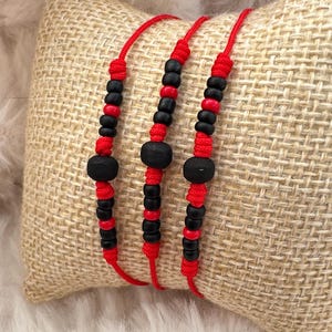 May include: Three red string bracelets with black beads and a larger black bead in the center of each bracelet.