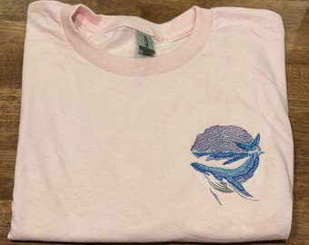 May include: A pink t-shirt with an embroidered design of two blue whales swimming in a circle.