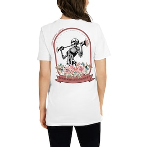 Puede incluir: Camiseta blanca con un gráfico rosa y negro de un esqueleto levantando pesas con flores y el texto "Strong women lift each other up".