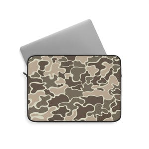 May include: A laptop sleeve with a camouflage pattern in shades of brown, tan, and beige. The sleeve is rectangular with a black zipper and a laptop partially inserted. The laptop is silver.