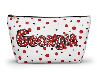 May include: White cosmetic bag with a black zipper and red and black polka dots. The word "Georgia" is printed in red with white polka dots and a black outline.