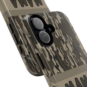 May include: Close-up of two phone cases with a camouflage pattern in shades of brown, tan, and black. The cases have a glossy finish and feature camera cutouts. The design includes a stripe with the word "MAMA" in white.