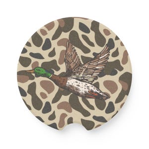 May include: A brown and green duck flying over a camouflage pattern background. The duck has a green head and a brown body with white spots.