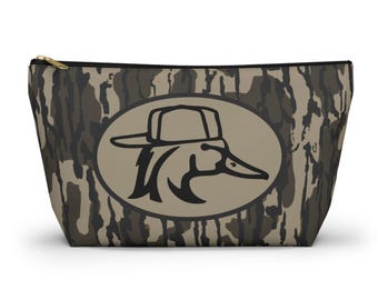 May include: A camouflage-patterned zippered pouch with a duck logo. The pouch features a brown, black, and gray camouflage design. The duck logo is in an oval shape and depicts a duck wearing a hat. The zipper is gold-colored.