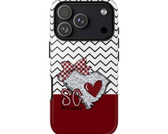 May include: A smartphone case featuring a black and white chevron pattern on the top half and a solid dark red bottom. The design includes a leopard print outline of South Carolina, a red plaid bow, a red heart, and the text SC SOUTH CAROLINA.