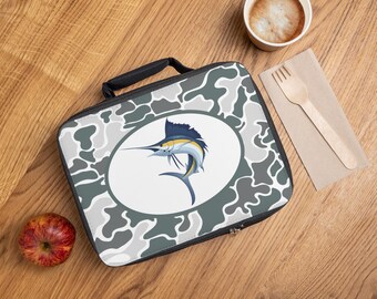 May include: A rectangular lunch bag featuring a gray and white camouflage pattern with a central white oval containing a blue and yellow marlin fish illustration. The bag has a black handle and a black zipper closure along the top edge.