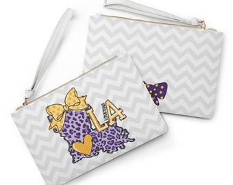May include: Two white wristlet pouches featuring a light gray chevron pattern. One pouch displays a purple leopard print map of Louisiana with a yellow polka-dot bow, a yellow heart, and the text LA. The other pouch shows a purple polka-dot bow.