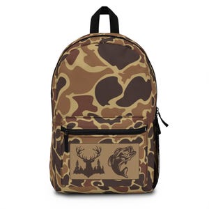 May include: A brown and tan camouflage backpack with a front pocket featuring a silhouette of a deer and a bass fish.