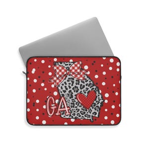 May include: A red laptop sleeve with a white polka dot pattern. The sleeve features a leopard print outline of the state of Georgia, a red heart, and a red and white gingham bow. The letters "GA" are also displayed.