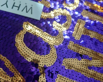 Puede incluir: Una superficie de tela cubierta con lentejuelas moradas y doradas, con el texto "WHY DRESS" impreso en una etiqueta rectangular blanca. Las lentejuelas están dispuestas para formar letras doradas sobre un fondo morado, creando una textura brillante.