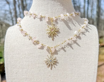 Puede incluir: Un delicado collar de cadena dorada con dos colgantes de estrella. La cadena está adornada con pequeñas piedras de cuarzo rosa claro.