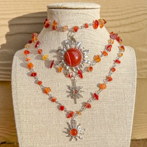Puede incluir: Un collar de tres capas con tres colgantes de sol de cornalina. El collar está hecho de plata y cuentas de cornalina. Las piedras de cornalina son de color naranja intenso.