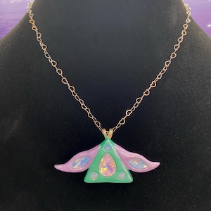 Puede incluir: Un collar con un colgante de tri&aacute;ngulo verde y morado con detalles iridiscentes que cuelga de una cadena de oro en forma de coraz&oacute;n.