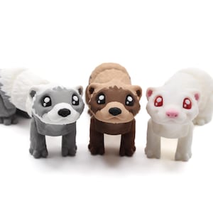 May include: Three ferret figurines in gray, brown, and white, each with large, expressive eyes. The gray ferret is lying down, while the other two stand upright. The figurines have a cartoonish style and are set against a white background.