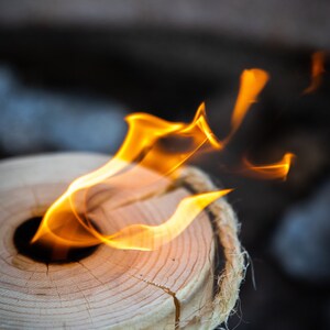 May include: A wooden log with rope wrapped around it, burning with a bright orange flame in the centre.